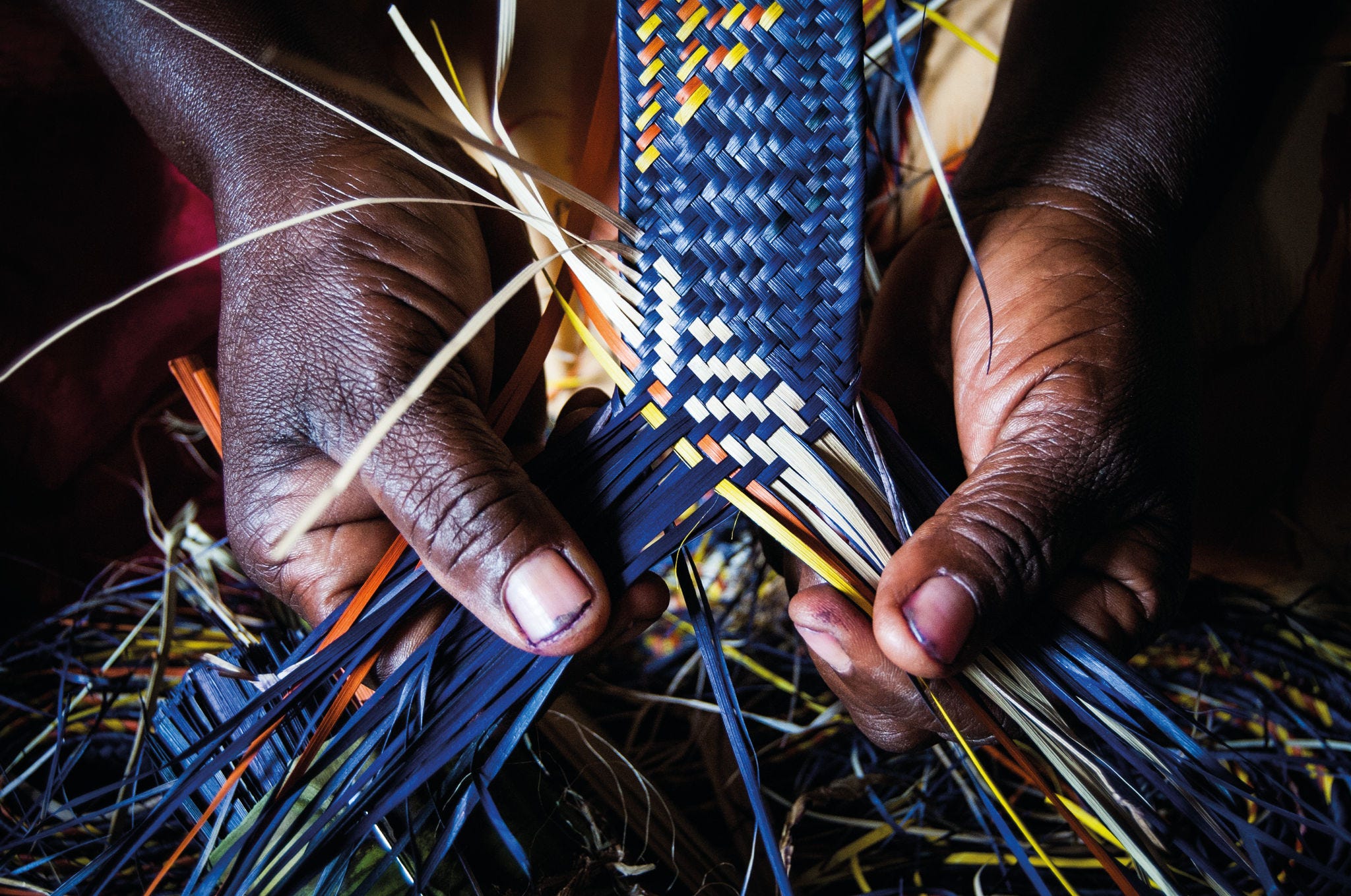  Detail of African woman's hands weaving blue and yellow raffia mat; Shutterstock ID 607227014; Nom de Projet : NetFWD