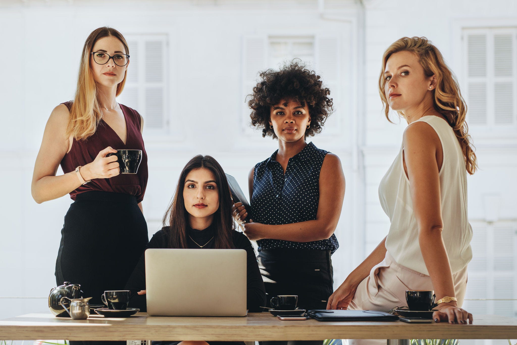 Group of businesswomen in casuals together at office desk and looking at camera